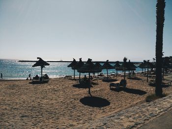 Silhouette people relaxing at beach against clear sky