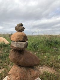 Stack of stones on field against sky