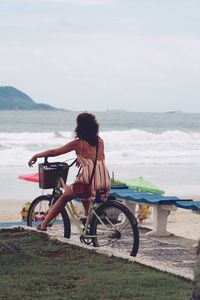 Side view of woman on bicycle on beach against sky