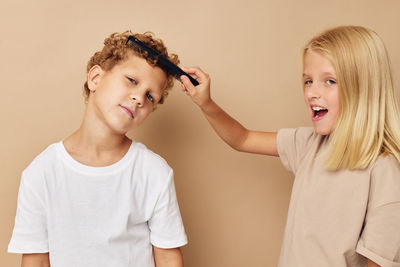 Girl combing hair of boy against beige background