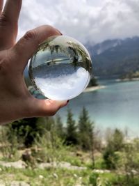 Cropped hand holding crystal ball against sky