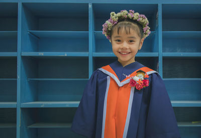 Portrait of smiling girl wearing flowers while standing against shelves