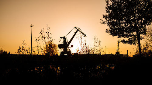 Silhouette of cranes on field against sky at sunset