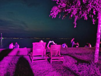 View of empty chairs by sea against sky at night