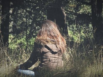 Side view of young woman sitting on tree in forest