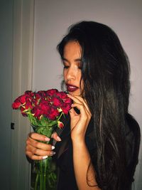 Young woman holding rose bouquet while standing against wall at home