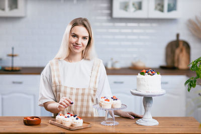 Portrait of smiling woman garnishing cake at kitchen