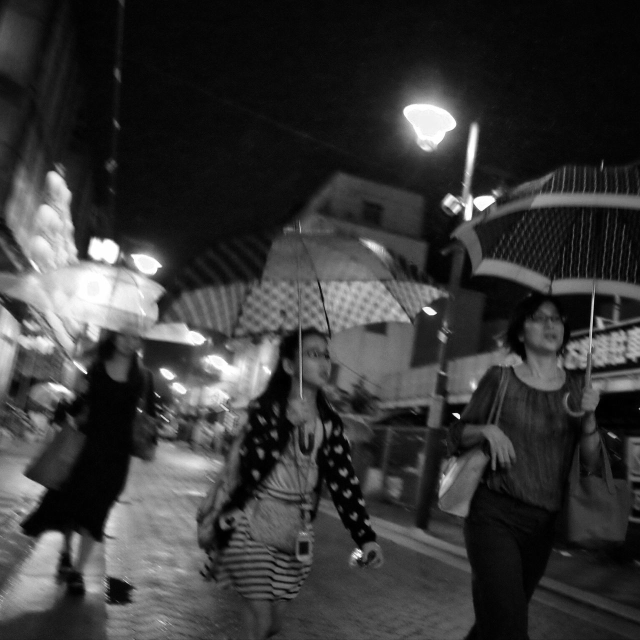 illuminated, street, walking, city, city life, night, blurred motion, travel, men, building exterior, lifestyles, city street, rush hour, large group of people, built structure, road, leisure activity, on the move, transportation, architecture, casual clothing, person, holding, mode of transport, selective focus, group of people, crowd