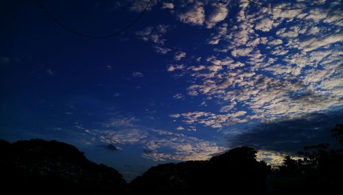 Low angle view of silhouette trees against blue sky