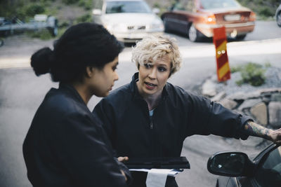 Female mechanic explaining customer while standing by car at auto repair shop