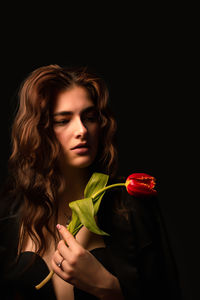 Portrait of young woman holding sparkler against black background