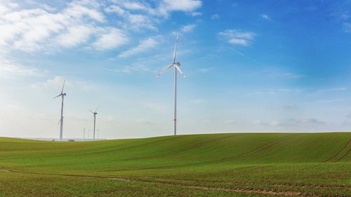 Scenic view of agricultural field against sky and wind turbines