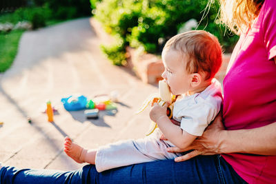 Baby girl eating banana while sitting with mother outdoors