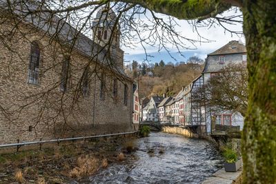 Bridge over river amidst houses and trees against sky