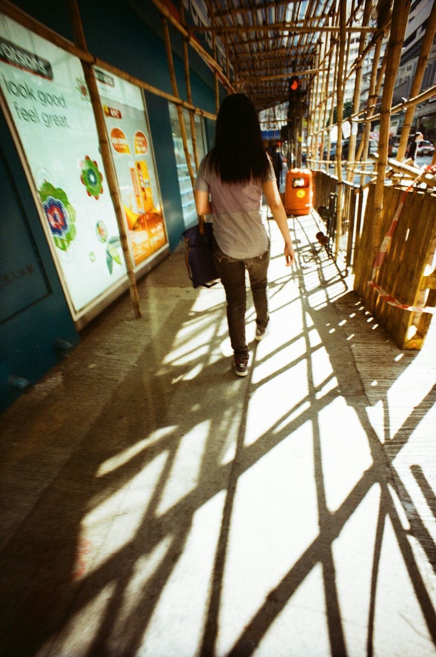 full length, indoors, lifestyles, walking, rear view, casual clothing, architecture, built structure, leisure activity, shadow, men, flooring, person, city life, wall - building feature, sunlight, the way forward