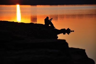 Silhouette men sitting on shore during sunset
