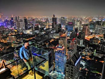 Man standing in balcony against illuminated cityscape and sky at night
