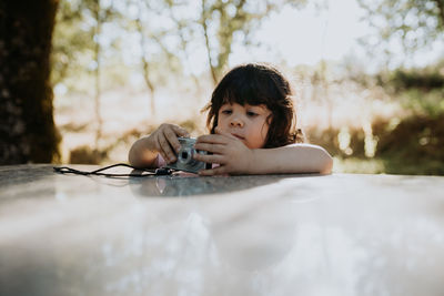 Portrait of boy holding camera against trees