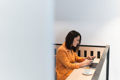 Side view of female freelancer browsing mobile phone while sitting at table in cafe and working on remote project