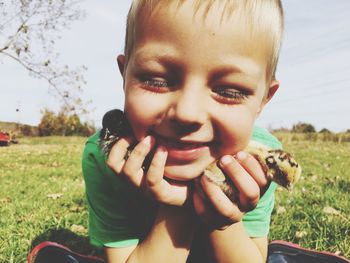 Close-up of smiling boy with baby chickens on field