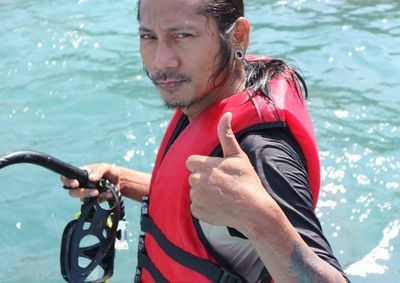 Portrait of man showing thumbs up sign while holding snorkel in sea on sunny day