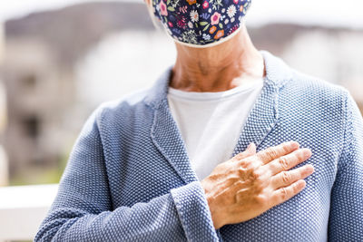 Midsection of senior woman wearing wearing mask gesturing while standing outdoors