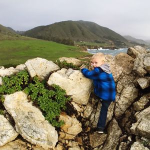 Full length portrait of boy climbing rocks against sky