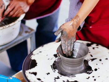 Midsection of people making pot on spinning wheel at workshop