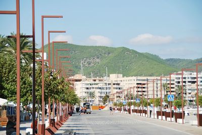 People on road by buildings in city against sky