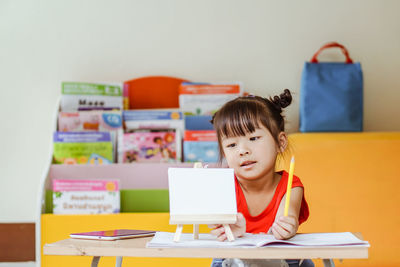 Cute girl drawing on paper while sitting on table at home