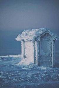 Snow covered outhouse against clear sky