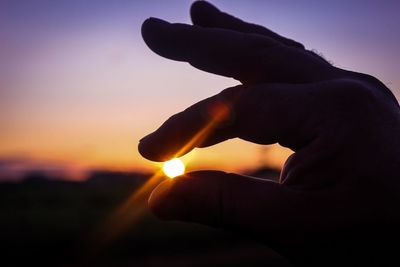 Close-up of human hand against sunset