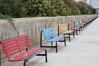 Empty bench on sidewalk against plants
