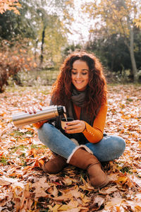 Young woman smiling while sitting on street during autumn