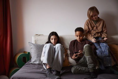 Children sitting on bed and using phones