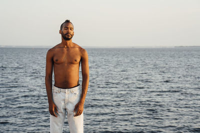 Shirtless man with eyes closed standing in front of horizon