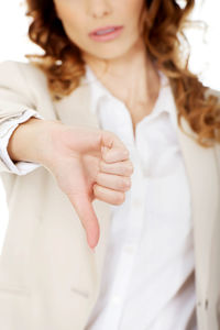 Midsection of businesswoman gesturing thumbs down sign against white background