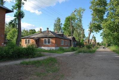 Road amidst trees and houses against sky