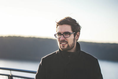 Young man wearing eyeglasses standing against sky