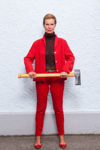 Portrait of woman holding axe standing against white wall