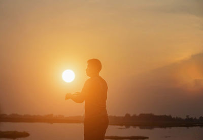 Silhouette man standing by lake against sky during sunset