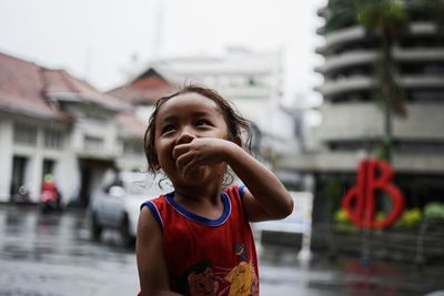 Close-up of smiling girl with finger in mouth against buildings