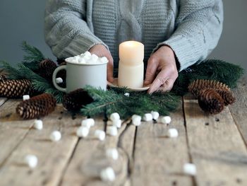 Burning candle in the hands of an elderly woman on the background of a wooden rustic table.