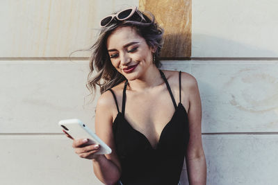 Young woman using mobile phone against wall