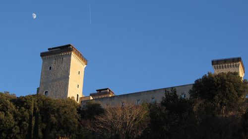 Low angle view of historic building against clear blue sky with clear moon and airplane