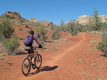 Woman riding bicycle on dirt road against sky