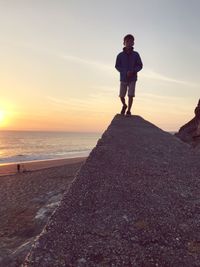 Boy walking on retaining wall at beach during sunset