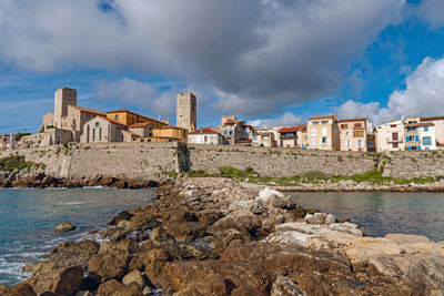 Buildings by sea against cloudy sky