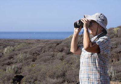 Man looking through binoculars at landscape against sky