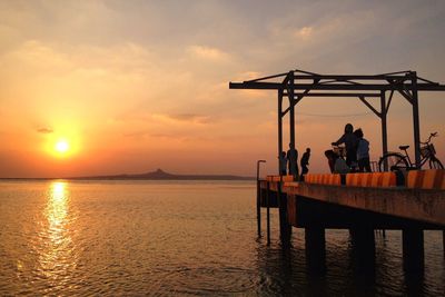 People on pier by sea against sky during sunset